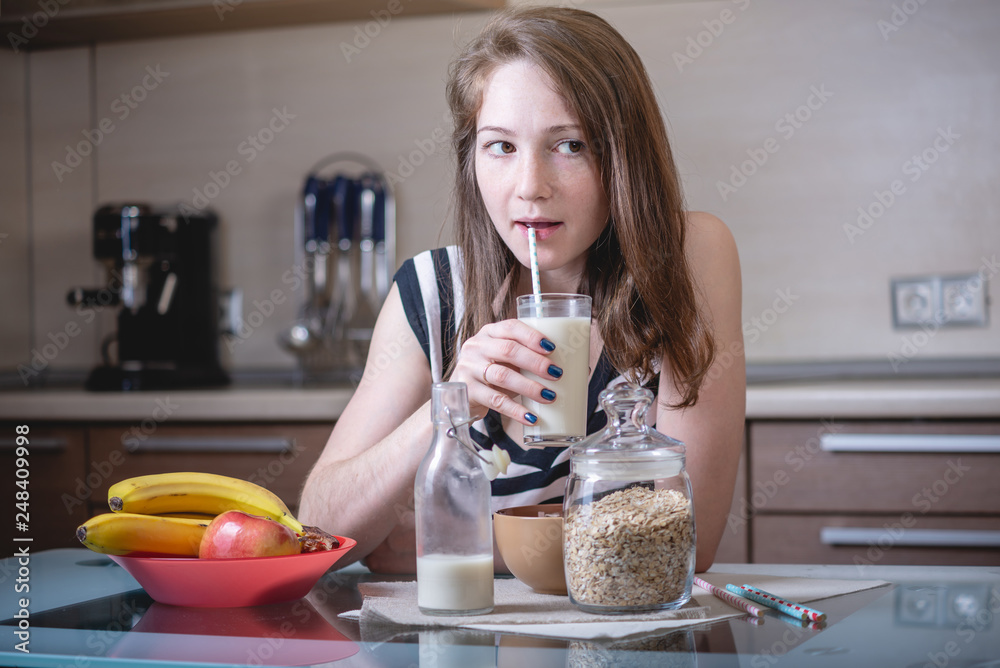 Woman drinking organic oat milk from straws holding a glass glass Cup in the kitchen. Diet healthy vegetarian product Woman drinking organic oat milk from straws holding a glass glass Cup in the kitchen. Diet healthy vegetarian product