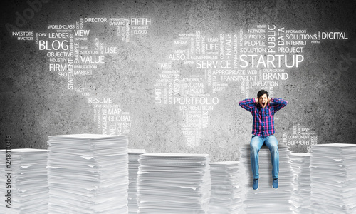 Attractive man sitting on pile of paper documents.