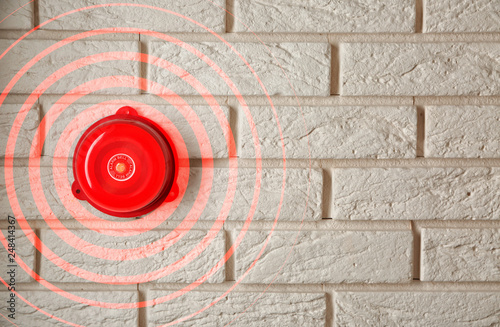 Modern alarm bell on brick wall indoors photo