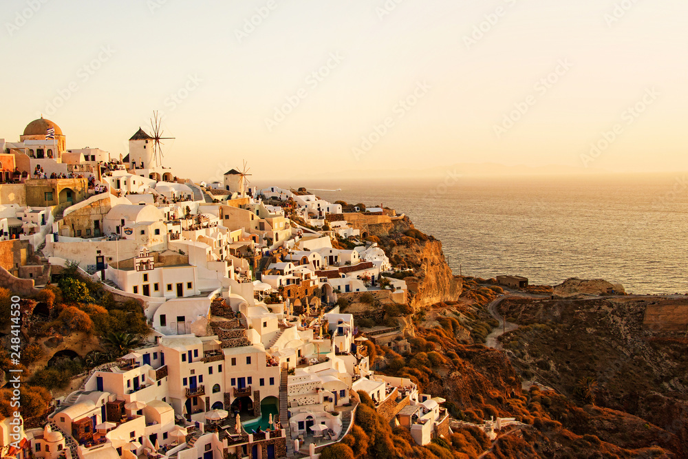 Two white old windmills on a background of white plastered houses at sunset in the town of Oia on Santorini island in Greece