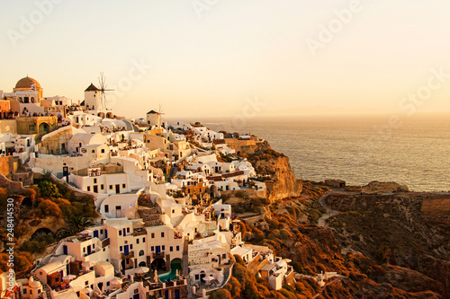 Two white old windmills on a background of white plastered houses at sunset in the town of Oia on Santorini island in Greece © zenobillis