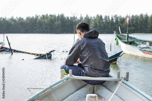 Young asian man sit on prow of finish boat at evening time. Travel and relaxation concept.