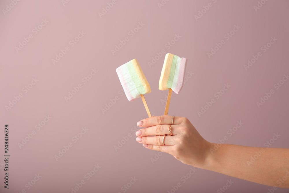 Female hand holding tasty marshmallow lollipops on color background Female hand holding tasty marshmallow lollipops on color background