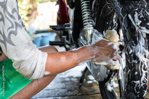 Close-up of hand of man worker washing motorcycle. Man cleaning motorcycle with sponge at car wash shop.