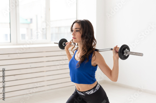 Sport, fitness and people concept - Beautiful young woman exercising squatting with barbell