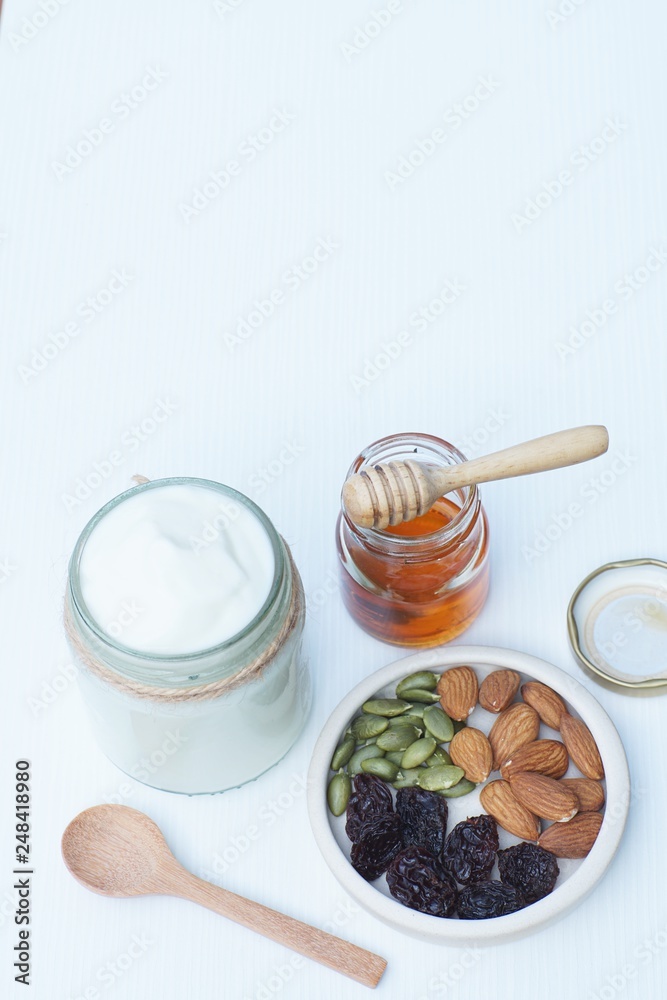 Fototapeta premium Plain yoghurt in white bowl, honey, cereal, raisin and wood spoon on white wooden table background
