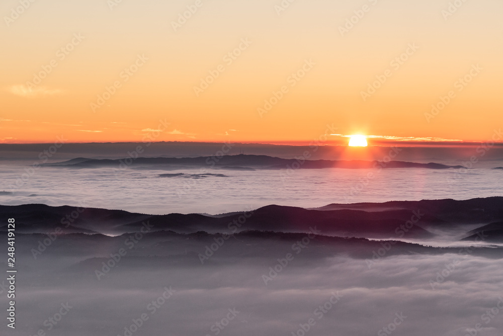 Beautiful sunset over a valley filled by fog with mountains and hills