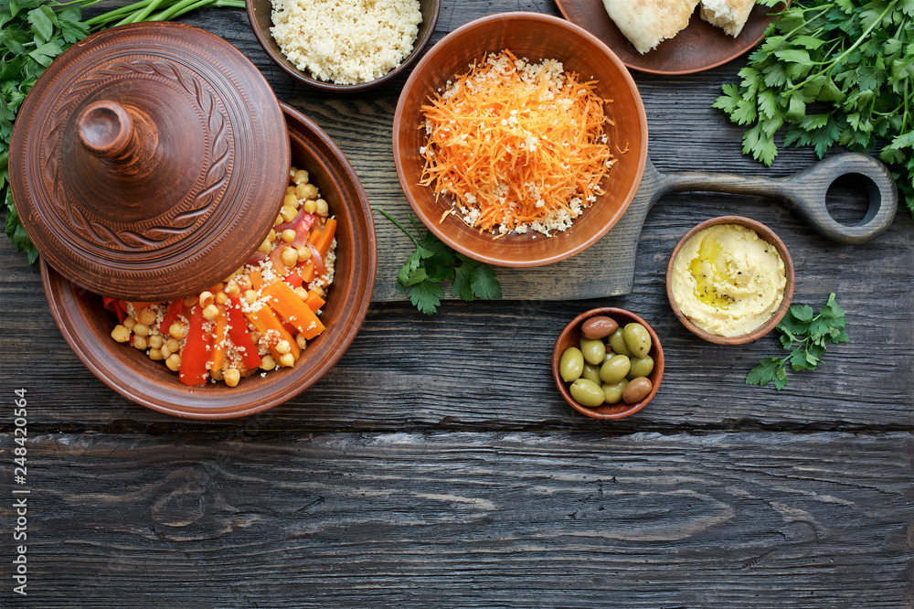 Moroccan traditional tajin and various snacks on dark wooden table. Carrot Salad, Couscous, Olives, Hummus. Flat lay Moroccan traditional tajin and various snacks on dark wooden table. Carrot Salad, Couscous, Olives, Hummus. Flat lay