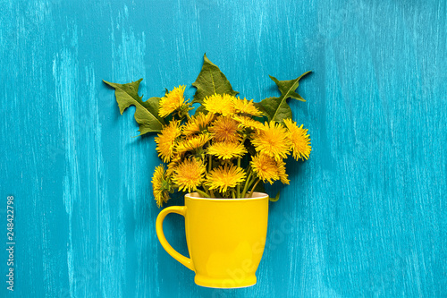 Bouquet dandelions taraxacum flowers in yellow mug on wood blue background Template for postcard, lettering, text or your design Flat lay Top view Concept Hello summer Creative top-down composition.