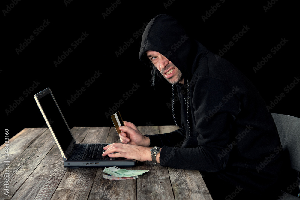 hacker in black hoody with laptop, bank card and euro notes hacker in black hoody with laptop, bank card and euro notes