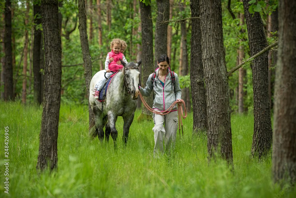 Girl having fun with mother and horse in the woods, young pretty girl with blond curly hair, freedom, joy, movement, outdoor, spring, healthy, happy family, cheerfull, kid on vacation