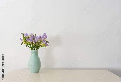 Purple freesia flowers in green vase on stone bench against white wall with copy space (selective focus) © Natalie Board