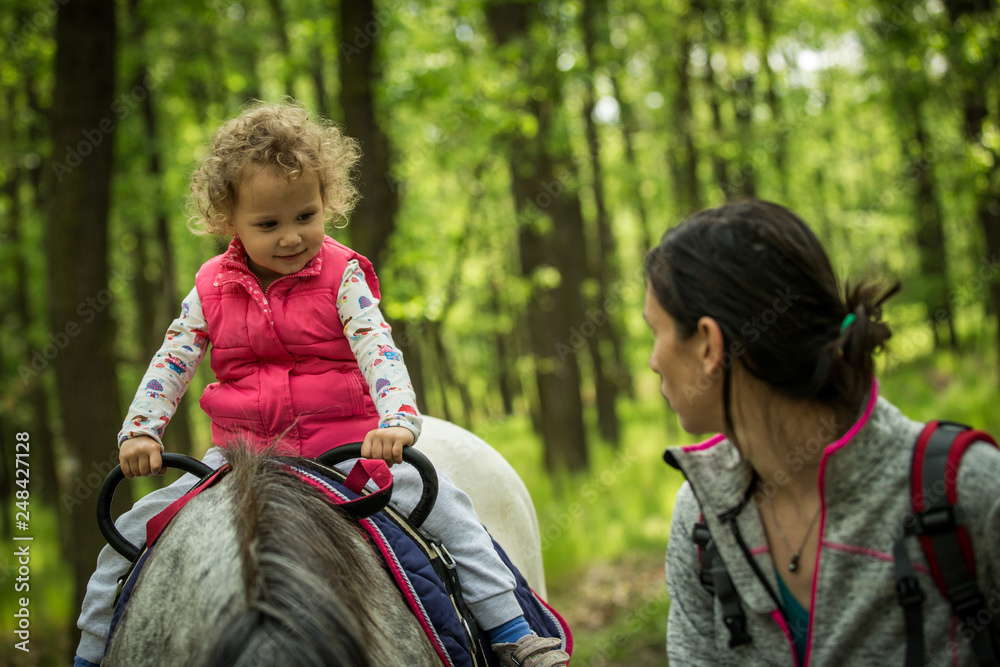 Girl having fun with mother and horse in the woods, young pretty girl with blond curly hair, freedom, joy, movement, outdoor, spring, healthy, happy family, cheerfull, kid on vacation Girl having fun with mother and horse in the woods, young pretty girl with blond curly hair, freedom, joy, movement, outdoor, spring, healthy, happy family, cheerfull, kid on vacation