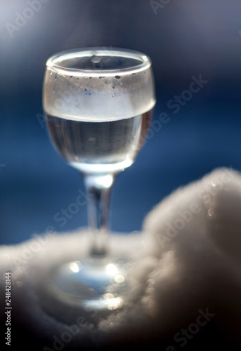 Glass wineglass with liquid standing on the snow with a blurred background