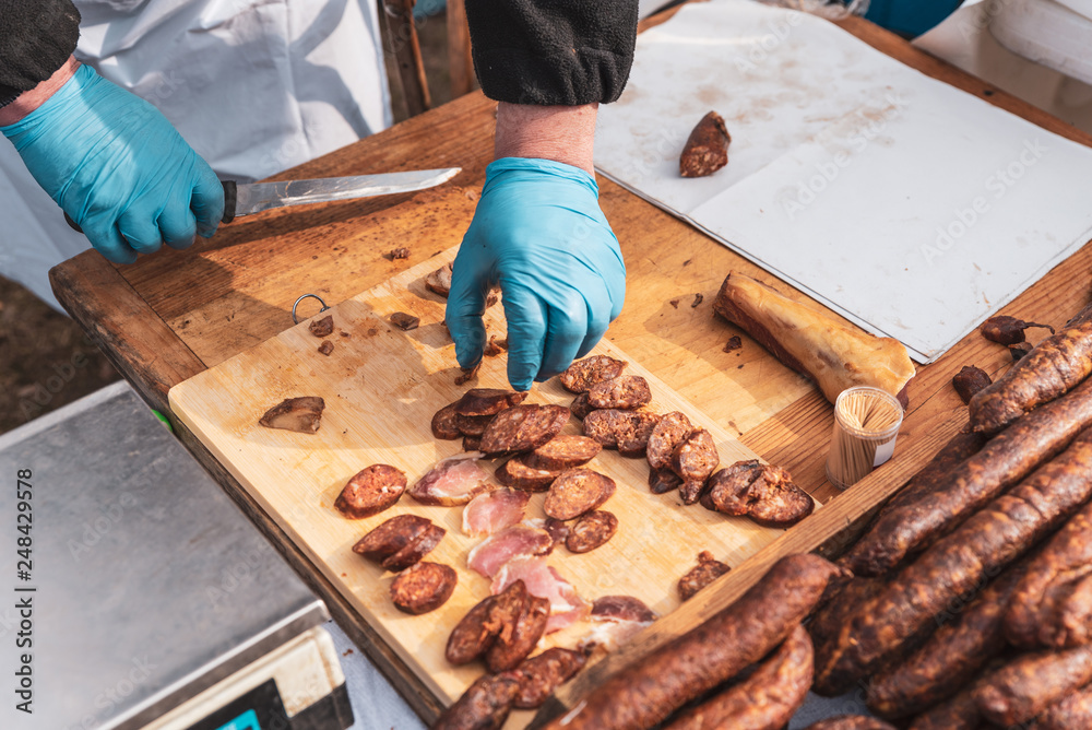 men's hands with gloves chop with a knife of a piece of sausage men's hands with gloves chop with a knife of a piece of sausage