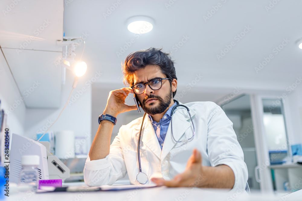 Male doctor in white coat is using a modern smartphone device