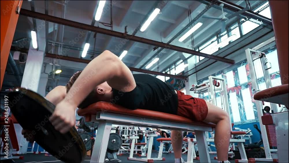 A young sports man in a black t-shirt is lying on the bench and doing an exercise with dumbbells. A young sports man in a black t-shirt is lying on the bench and doing an exercise with dumbbells.