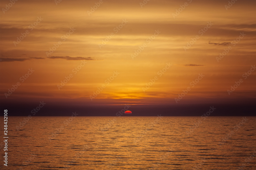Beautiful sea orange sunset with sun on the horizon and cloudy sky