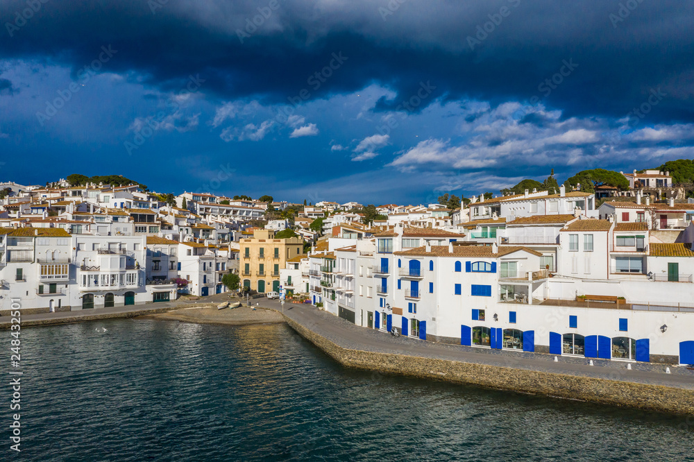 Aerial drone view of Cadaques tourist Holiday destination in Spain. Streets with white houses. walking mood. Sunny day with dark blue cloudy sky