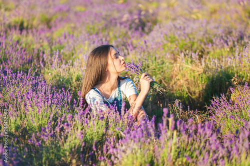 Young beautiful girl sits on a lavender meadow with a bouquet of flowers in their hands