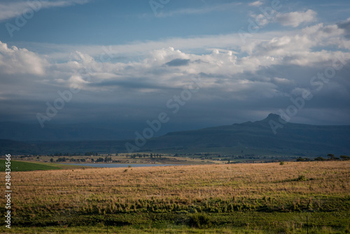 A grassy plain and hazy mountains in the distance  lit up by the late evening sun. Drakensberg  South Africa