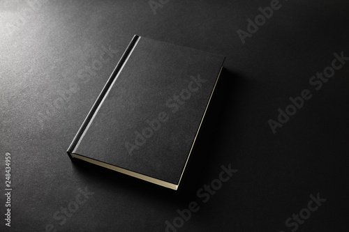 Mockup of closed blank black book on black paper background.
