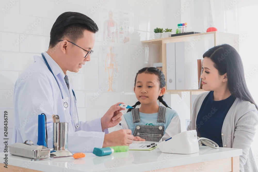 Professional doctor wearing white coat using thermometer to examine kid patient with her mother in hospital background.Concept of disease treatment and health care in hospitals. Professional doctor wearing white coat using thermometer to examine kid patient with her mother in hospital background.Concept of disease treatment and health care in hospitals.