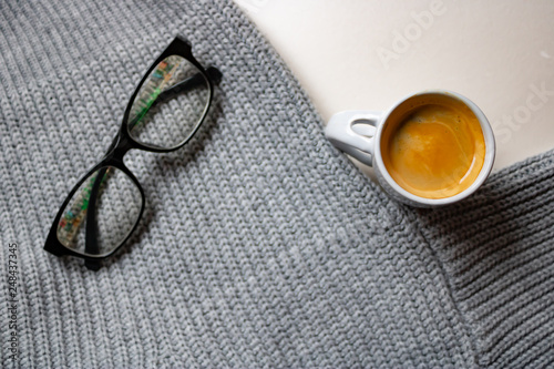 White espresso cup near the grey sweater with the glasses