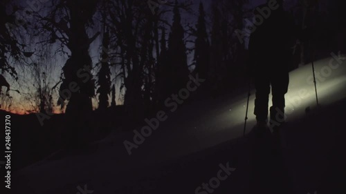 A man skiing in a night snowy forest with a flashlight, rear view. Dolly shot skitour in Siberia