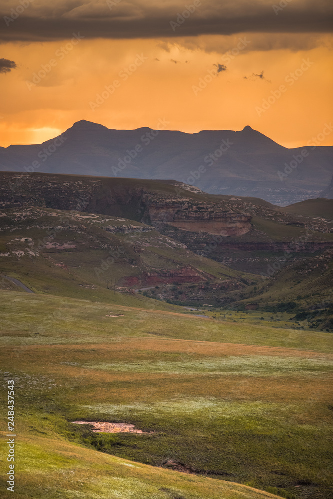 Dramatic storm clouds glow gold at sunset over the Drakensberg mountains surrounding the Amphitheatre, seen from Golden Gate Highlands National Park in the Drakensberg, South Africa