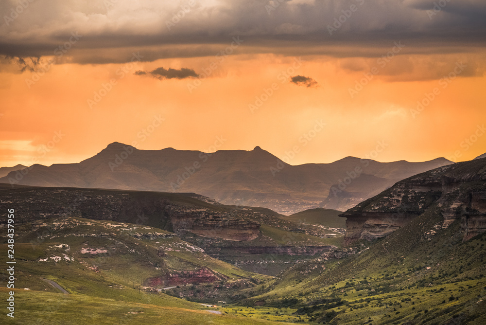 A dramatic scene of golden sunset and storm clouds over the Drakensberg mountains surrounding the Amphitheatre, seen from Golden Gate Highlands National Park in the Drakensberg, South Africa