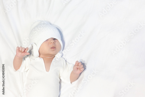 Curious little baby boy wearing white knitted hat and lying on white