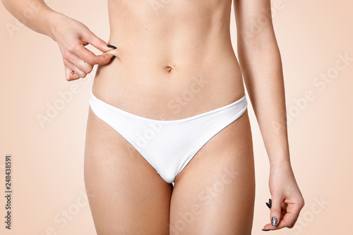 Body care and weight loss concept. Cropped shot of womans belly, holds skin, checks cellulite, gets rid of fat, wears white panties, has healthy skin, isolated over beige background. Females torso