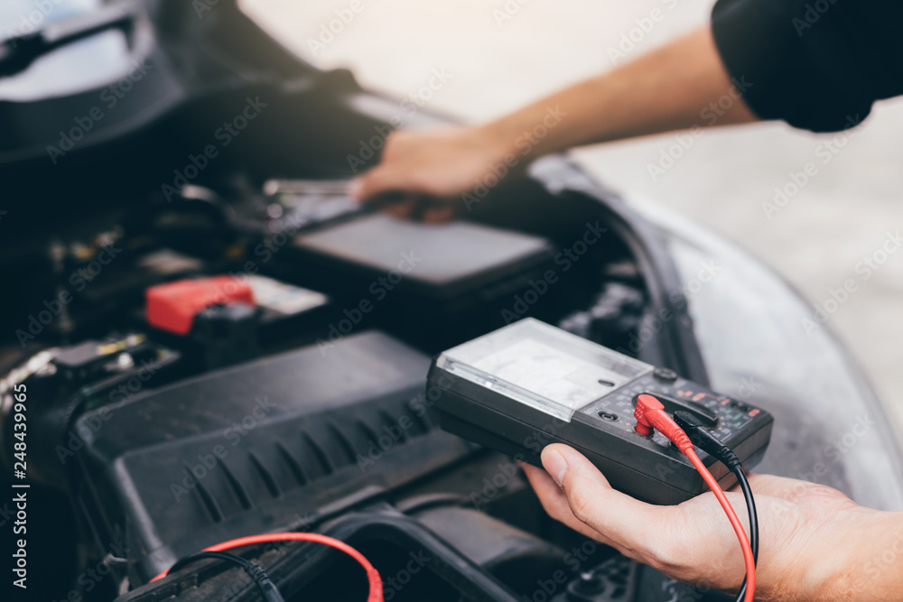 The car mechanic is carrying a battery meter and checking the general condition of the engine.