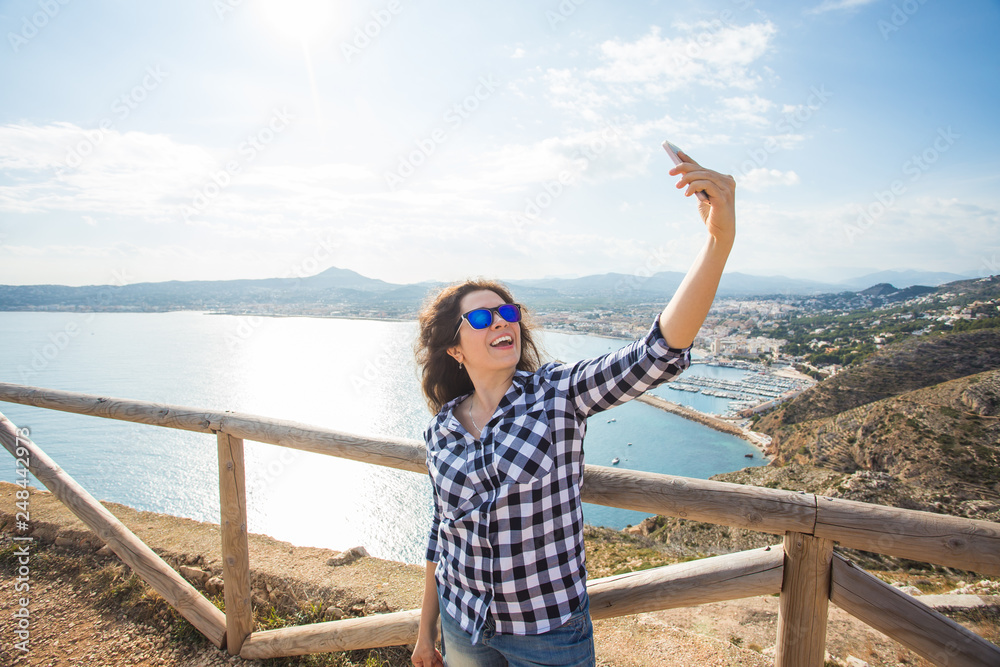 Travel, tourism and vacation concept - Happy young woman taking selfie near a sea
