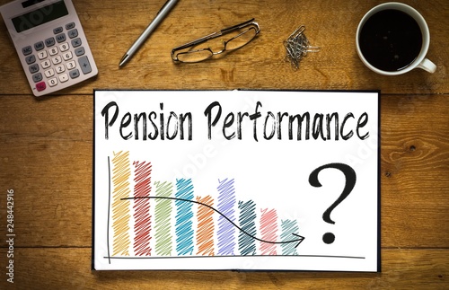 Overhead top view of Pension Performance written in book on desk with a coloured bar chart and trend line.  Desk has coffee cup, glasses, pen and calculator photo