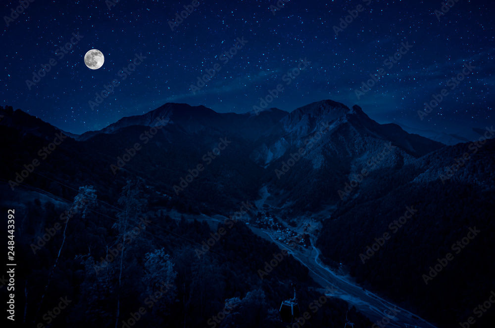 Fototapeta premium Mountain Road through the forest on a full moon night. Scenic night landscape of dark blue sky with moon. Azerbaijan