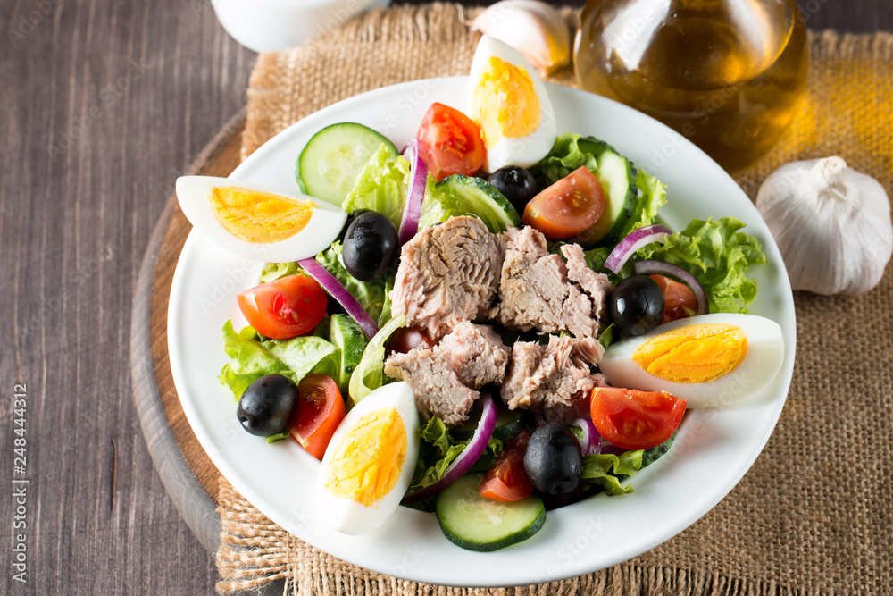 Fresh fish tuna salad made of tomato, ruccola, tuna, eggs, arugula, crackers and spices. Caesar salad in a white bowl on wooden background Fresh fish tuna salad made of tomato, ruccola, tuna, eggs, arugula, crackers and spices. Caesar salad in a white bowl on wooden background