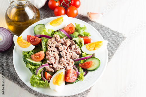 Fresh fish tuna salad made of tomato, ruccola, tuna, eggs, arugula, crackers and spices. Caesar salad in a white bowl on wooden background
