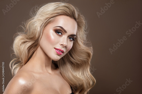 Blonde haired Woman Portrait with blue eyes and Healthy Long Shiny Wavy hairtyle. Volume shampoo. Blond Curly permed Hair and bright makeup. Beauty salon and haircare concept.