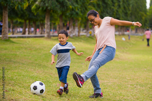 happy Asian Indonesian mother playing football with little 5 years old son running together excited laughing having fun in soccer fan child and healthy lifestyle education