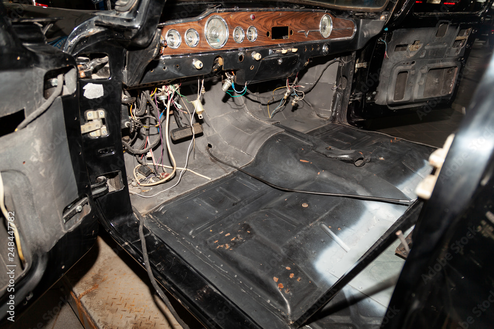 Disassembled car body, inside a black sedan, with parts and interior elements removed, prepared for the restoration and replacement of sound insulation and interior trim.