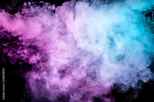 Translucent, thick smoke, illuminated by light against a dark background, divided into three colors: blue, green and purple, burns out, evaporating from a steam of vape.