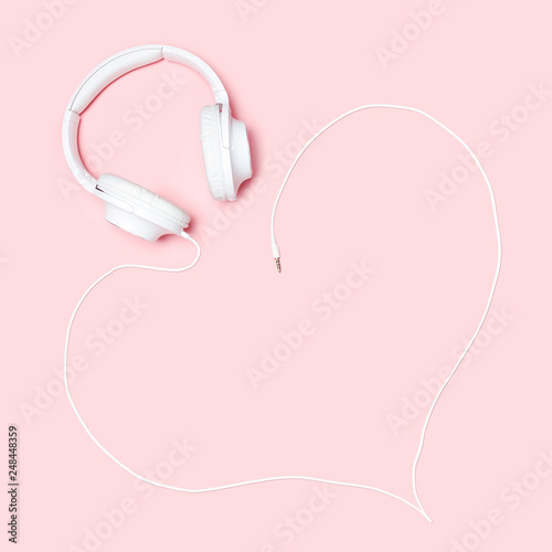 Headphones with a cord in the shape of a heart on pink background. Minimalistic flat lay composition with copy space for bloggers, designers, magazines etc.