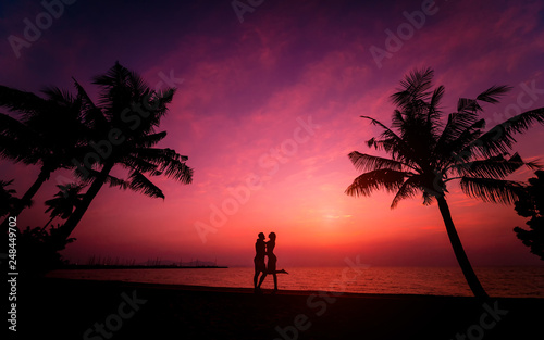 Silhouette of couple on tropical beach during sunset on background of palms and sea