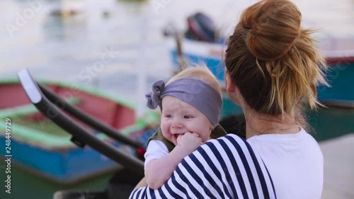 A newborn child gnawing fingers, a mother sitting on the bench and looking away with her yearling daughter near the sea