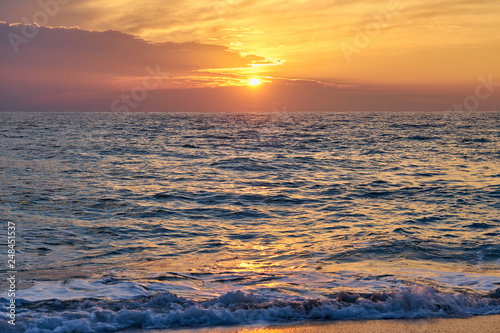 Tropical beach. Colorful sunset seascape. Waves with foam hitting sand.