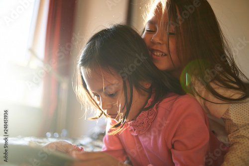 Two cute young Asian sisters lying on the bed playing together with a mobile device 