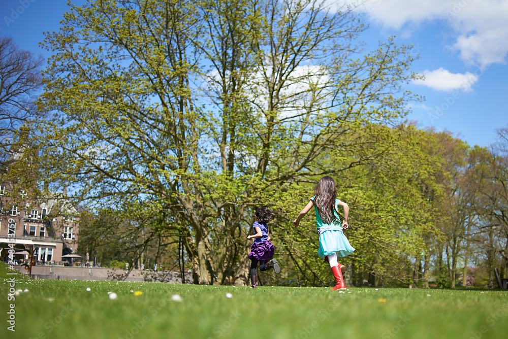 Fototapeta premium Cute Asian girl running around and playing in a big field surrounded by trees and nature in spring sunshine