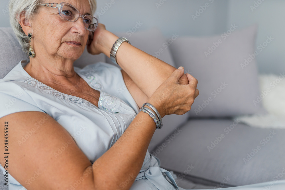 Senior woman suffering from pain in hand at home. Old age, health problem and people concept Senior woman suffering from pain in hand at home. Old age, health problem and people concept
